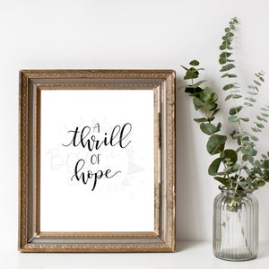 Puede incluir: Una impresi&oacute;n enmarcada con un marco dorado y un fondo blanco. La impresi&oacute;n presenta una caligraf&iacute;a negra que dice "a thrill of hope".