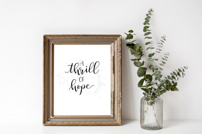 Puede incluir: Una impresi&oacute;n enmarcada con un marco dorado y un fondo blanco. La impresi&oacute;n presenta una caligraf&iacute;a negra que dice "a thrill of hope".