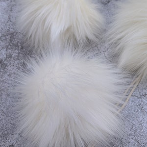 May include: Three white fluffy pom poms, perfect for adding a touch of whimsy to hats, scarves, or other crafts.