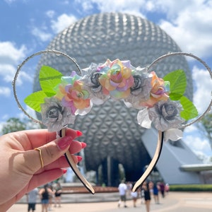 Op de afbeelding: Zilveren glitter muis oren met een bloemenhoofdband met pastel roze, blauwe en gele rozen en groene bladeren. De oren zijn voor een zilveren geodetische koepel.