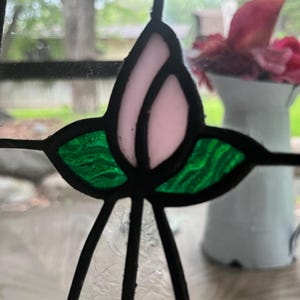 May include: A stained glass panel featuring a central light pink tulip bud motif flanked by two textured green leaves. The individual glass pieces are joined together by dark lead cames, creating a clear geometric floral design.