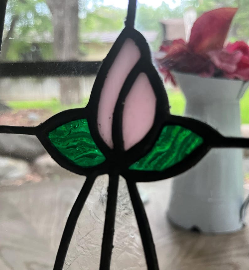 May include: A stained glass panel featuring a central light pink tulip bud motif flanked by two textured green leaves. The individual glass pieces are joined together by dark lead cames, creating a clear geometric floral design.