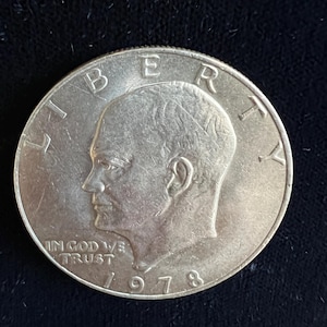 May include: Silver US dollar coin with the profile of a man on the front. The coin says "Liberty" around the edge and "In God We Trust" and "1978" below the profile.