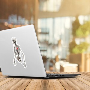Peut inclure: Un ordinateur portable blanc avec un autocollant repr&eacute;sentant un squelette avec un c&oelig;ur rouge dans la poitrine.