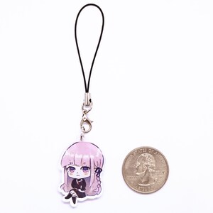 May include: A pink and black anime character phone charm with a black lanyard. The charm is about the size of a US quarter.