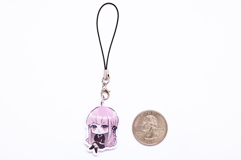 May include: A pink and black anime character phone charm with a black lanyard. The charm is about the size of a US quarter.
