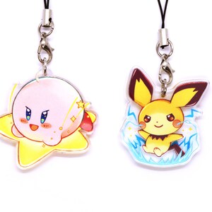 May include: Two colorful character charms on black lanyards with silver clasps. The charm on the left is pink and yellow and features a cartoon character with a star shape. The charm on the right is yellow and blue and features a cartoon character with lightning bolts.