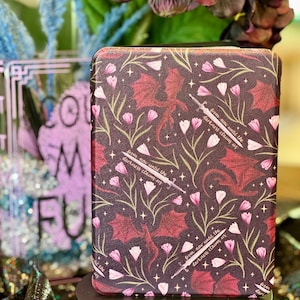 May include: A black phone case with a repeating pattern of pink flowers, red dragons, and gold swords. The text "from now until the darkness claims us" is repeated throughout the design.