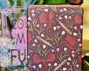 May include: A black phone case with a repeating pattern of pink flowers, red dragons, and gold swords. The text "from now until the darkness claims us" is repeated throughout the design.