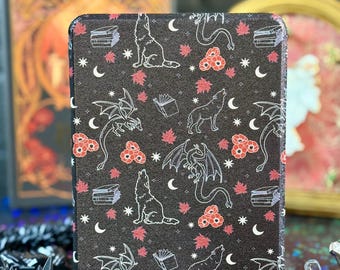 May include: Black e-reader cover with a repeating pattern of white wolves, dragons, books, moons, and red floral accents. The cover is rectangular and likely made of a durable material, designed to protect the device.