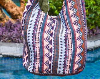 May include: A colorful, patterned, woven shoulder bag with a long strap. The bag is made of a soft, textured fabric and has a geometric design in shades of pink, blue, brown, and purple.