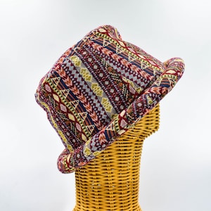 May include: A colourful, patterned bucket hat with a geometric design in shades of red, blue, green, and yellow. The hat is displayed on a wicker mannequin head.