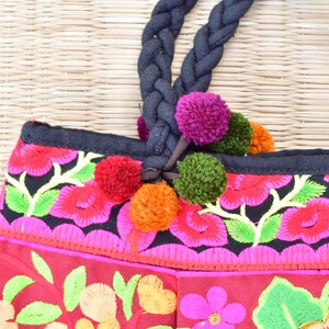 May include: A red and black embroidered tote bag with colorful pom-poms attached to the handles. The bag has a floral design with pink, green, yellow, and orange flowers.