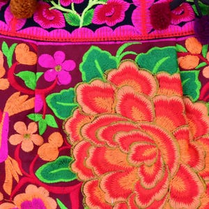 May include: Close-up of a vibrant embroidered fabric with a large red, orange, and pink flower in the center. The fabric is decorated with a variety of other flowers in shades of pink, green, and orange.