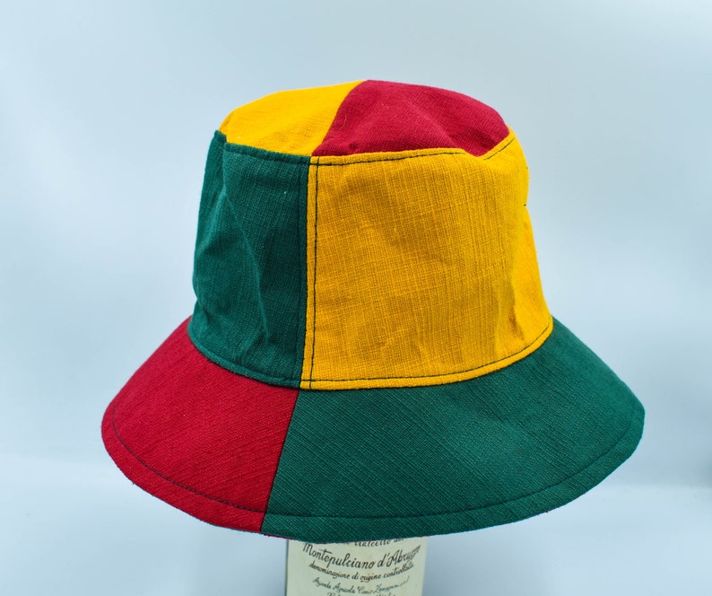 May include: A green, red, and yellow bucket hat. The hat is made of a woven fabric and has a wide brim.