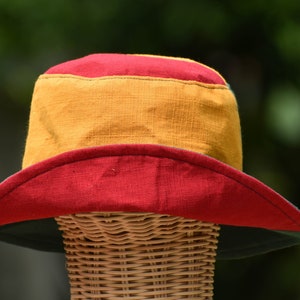 May include: A wide-brimmed hat with a red, yellow, and green color scheme. The hat is made of a soft, woven fabric and has a wide brim that can be folded down.