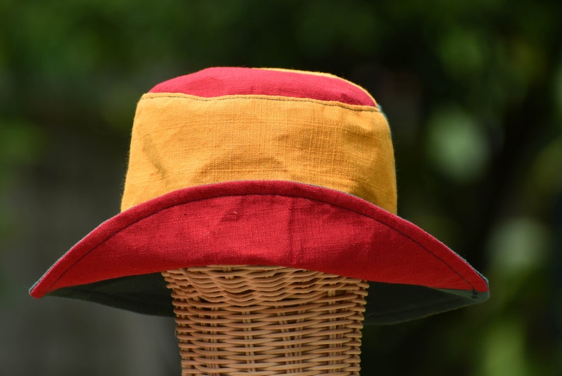 May include: A wide-brimmed hat with a red, yellow, and green color scheme. The hat is made of a soft, woven fabric and has a wide brim that can be folded down.