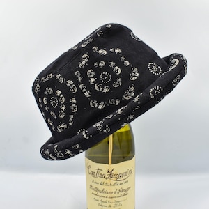以下が含まれることがあります： 黒いフェドラハット。白い模様が繰り返されています。ワインボトルの上に乗っています。短いブリムと丸みを帯びたクラウンがあります。柔らかい素材で作られています。