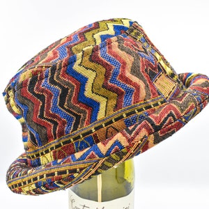 May include: A colorful, patterned hat with a zig-zag design in shades of red, blue, yellow, and black. The hat has a rounded crown and a rolled brim. The hat is made of a woven fabric.