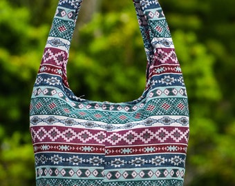 May include: A colorful, patterned, woven shoulder bag with a long strap. The bag is made of a soft, textured fabric and has a geometric design in shades of red, blue, green, and white.