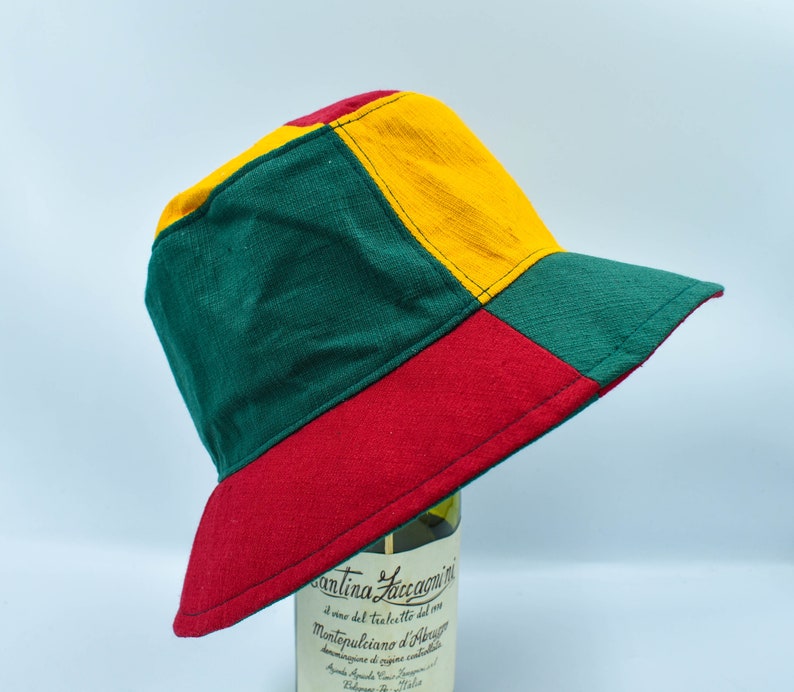 May include: A green, yellow, and red bucket hat with a contrasting stitch detail. The hat is made of a soft, textured fabric.