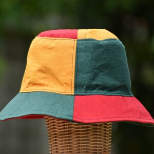 May include: A colorful bucket hat with a green, red, and yellow patchwork design. The hat is made of a soft, woven fabric.
