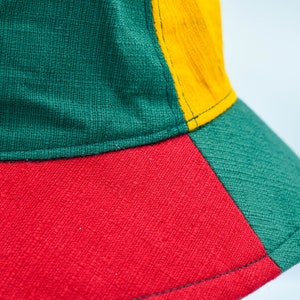 May include: A green, red, and yellow bucket hat. The hat is made of a woven fabric.