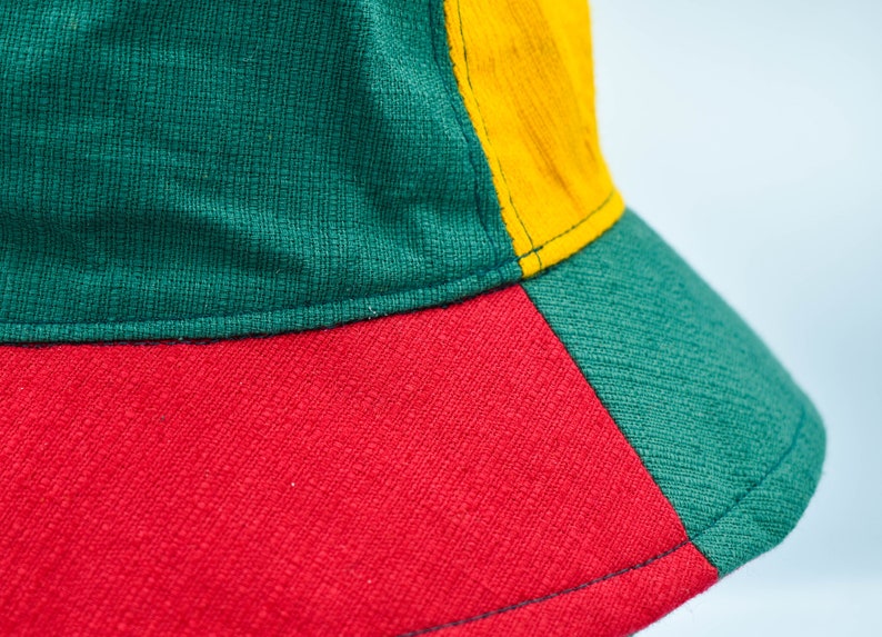 May include: A green, red, and yellow bucket hat. The hat is made of a woven fabric.