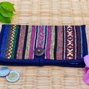 May include: A colorful, rectangular wallet with a woven fabric design in shades of blue, green, yellow, pink, and maroon. The wallet has a dark blue border and a wooden button closure. Two coins are visible near the wallet.