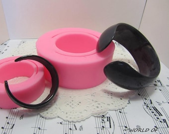 May include: Two pink silicone molds for making bracelets, one large and one small, with a black plastic bracelet on a white lace doily.