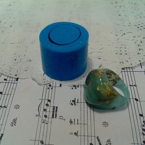 May include: A blue silicone mold for making rings, and a green resin ring with gold flakes.