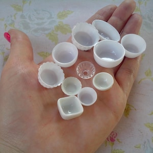 Könnte beinhalten: Eine Hand hält eine Sammlung kleiner weißer Keramikschalen und -tassen. Die Schalen sind in verschiedenen Formen und Größen und einige haben einen gewellten Rand.