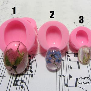 Könnte beinhalten: Drei rosa Silikonformen zum Gießen von Harz, nummeriert 1, 2 und 3. Jede Form ist oval und hat eine glatte, glänzende Oberfläche. Die Formen werden mit Harzgussteilen gezeigt, die gepresste Blumen enthalten.