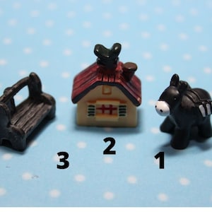 Peut inclure: Une figurine miniature d'âne noir, un petit banc en bois noir et une maison miniature au toit rouge avec un oiseau sur le dessus. La maison est jaune avec des fenêtres blanches et une cheminée rouge.