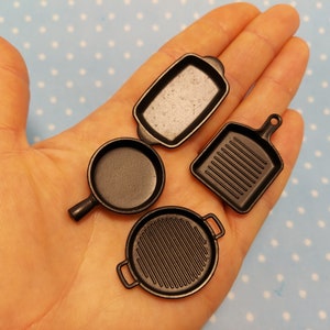 May include: Four miniature black frying pans, including a square grill pan, a round grill pan, a small frying pan, and a rectangular pan.