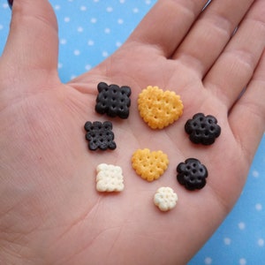 May include: A collection of eight miniature food charms, including heart-shaped, square, and round shapes. The charms are in black, white, and yellow.