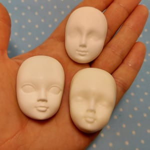Può includere: Tre teste di bambola in ceramica bianca con tratti del viso dipinti. Le teste sono lisce e hanno una finitura opaca.