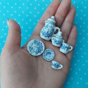 May include: A miniature tea set with a blue and white floral pattern. The set includes a teapot, creamer, sugar bowl, and two saucers.