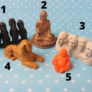 May include: A set of five small figurines, including a group of four black statues, a golden Buddha, a sphinx, a white sculpture of Mount Rushmore, and an orange Buddha.
