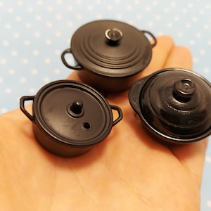以下が含まれることがあります： 蓋と取っ手がついた黒いミニチュア鍋が3つ。鍋は滑らかで光沢のある素材でできており、わずかに丸みを帯びた形をしています。