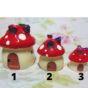 Peut inclure: Trois maisons champignons miniatures, peintes en rouge et blanc avec des pois blancs. Les maisons sont de tailles différentes, la plus grande étant étiquetée "1", la maison du milieu étant étiquetée "2" et la plus petite étant étiquetée "3".