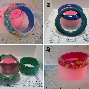 Pode incluir: Quatro moldes de silicone para fazer pulseiras de resina. Os moldes são cor de rosa e mostram as pulseiras de resina acabadas em várias cores, incluindo turquesa, verde, azul e vermelho. Algumas pulseiras têm flocos dourados embutidos na resina.