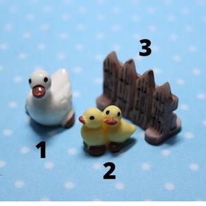 Op de afbeelding: Een wit eendje, twee gele eendjes en een bruin houten hek. De figuurtjes zijn klein en perfect voor een miniatuurtuin of een feeëntuin.