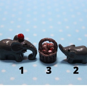 May include: Three miniature gray elephants, one with a red apple on its head, and a small brown basket filled with red and white mushrooms. The elephants are numbered 1, 2, and 3.