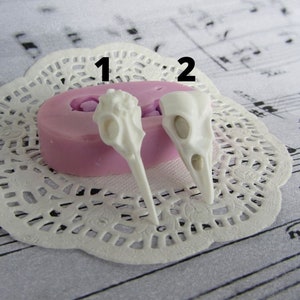 May include: Two white silicone molds for making bird skull shapes. The molds are on a white doily. The molds are numbered 1 and 2.