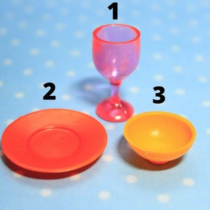 Può includere: Un set di tre piatti in plastica in miniatura: un bicchiere di vino rosa, un piatto arancione e una ciotola gialla.