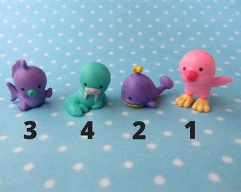 May include: Five small plastic figurines of sea creatures. A pink bird with yellow feet, a purple whale with a yellow fin, a teal walrus, a purple fish with a fin, and a pink bird with yellow feet.