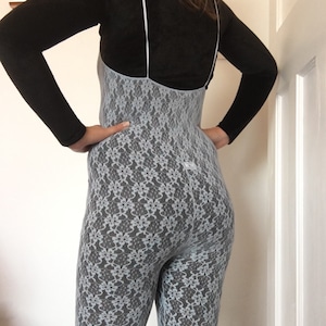 Könnte beinhalten: Ein schwarzes Langarm-Oberteil kombiniert mit einem hellblauen Spitzen-Jumpsuit. Der Jumpsuit hat ein Blumenmuster und dünne Träger. Das Outfit ist figurbetont und scheint aus einem weichen, dehnbaren Material zu sein.