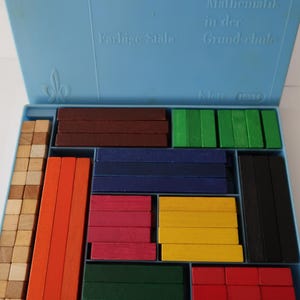 Könnte beinhalten: Eine blaue Kunststoffbox mit farbigen Holzblöcken für Bildungszwecke. Die Blöcke sind in verschiedenen Farben wie Rot, Gelb, Grün, Blau und Braun gehalten. Auf der Box steht "Mathematik in der Grundschule" und "Farbige Stäbe".