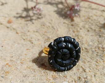 May include: A black and white ring with a spiral design. The ring is made of polymer clay and has a gold band.